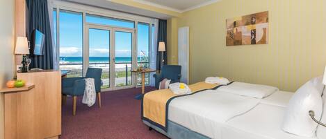 Una camera d'albergo con un letto, una scrivania con un computer, una sedia, un tavolo con una lampada e vista sull'oceano.