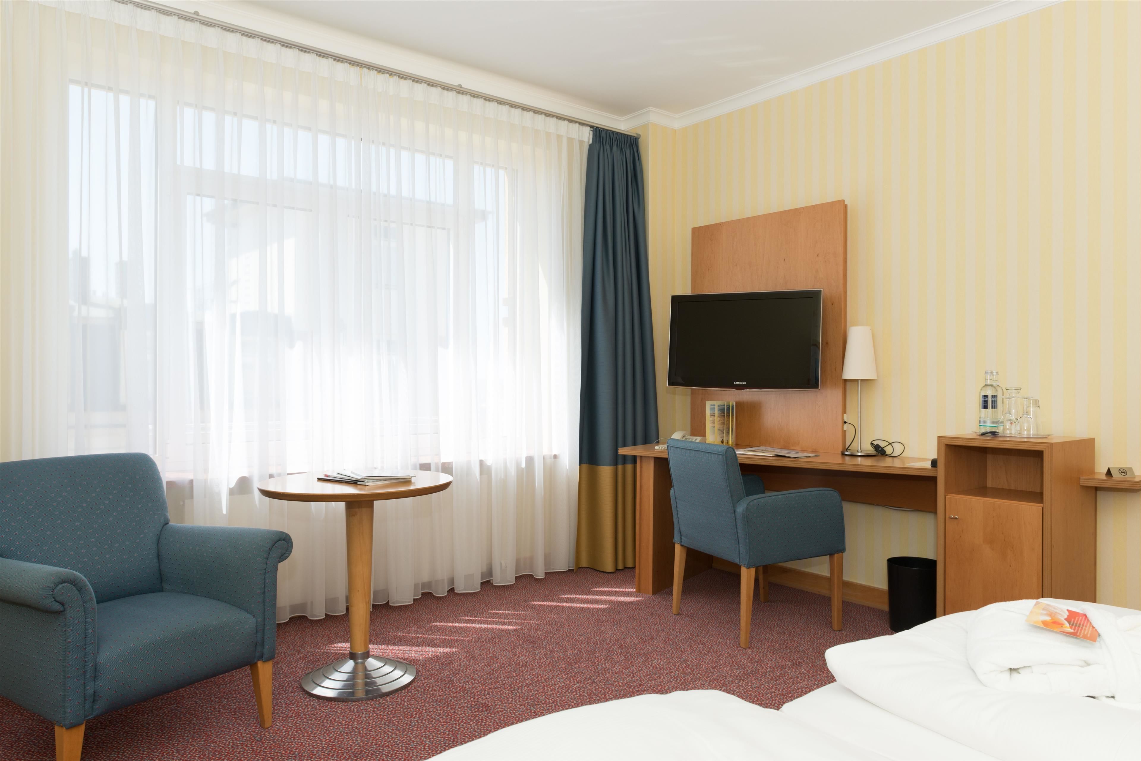 Ein Hotelzimmer mit Bett, Schreibtisch mit Stuhl, Fernseher und einem kleinen Tisch.