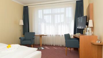Habitación de hotel con cama, dos sillones, una mesita, un escritorio con computadora y teléfono, televisor y ventana con cortinas.