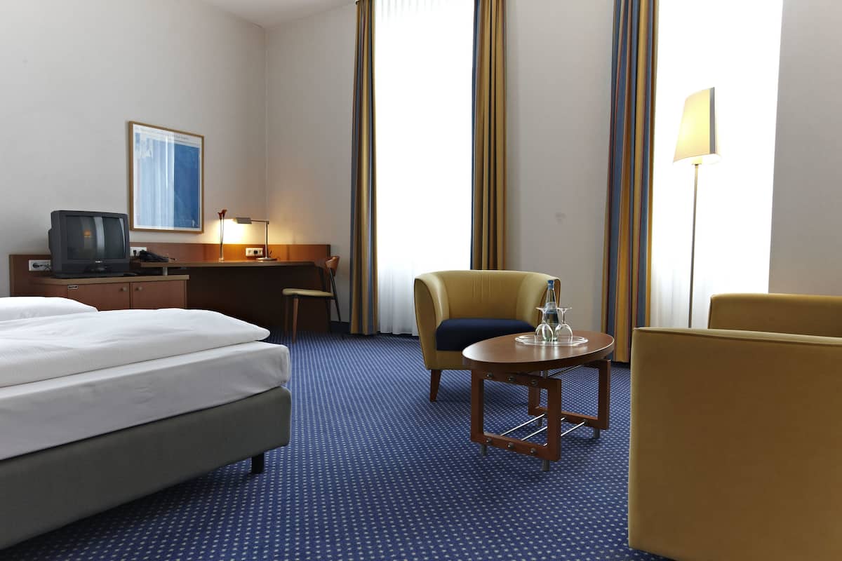 A hotel room with a bed, a desk, a chair, a table, and a television.