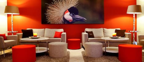 A modern lounge area with two sofas, red ottomans, and a large wall-mounted artwork of a bird.