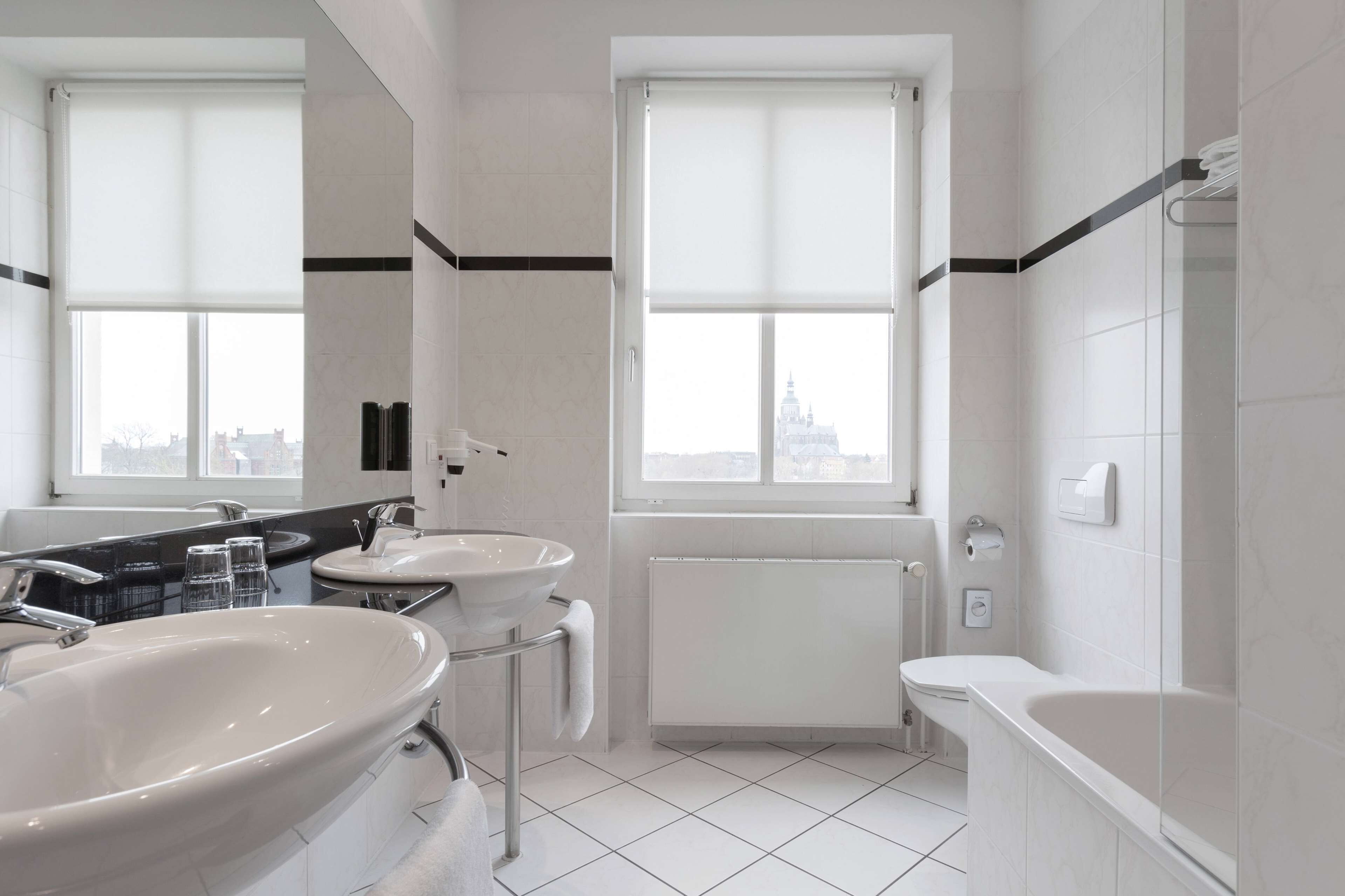 A modern bathroom with two sinks, a bathtub, and a window with a city view.