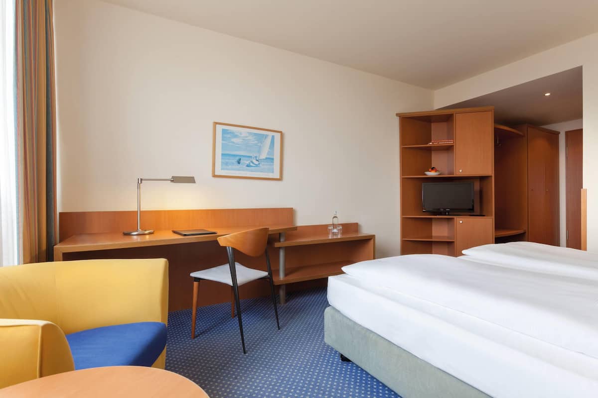 A hotel room with a bed, desk, chair, TV, and a painting on the wall.