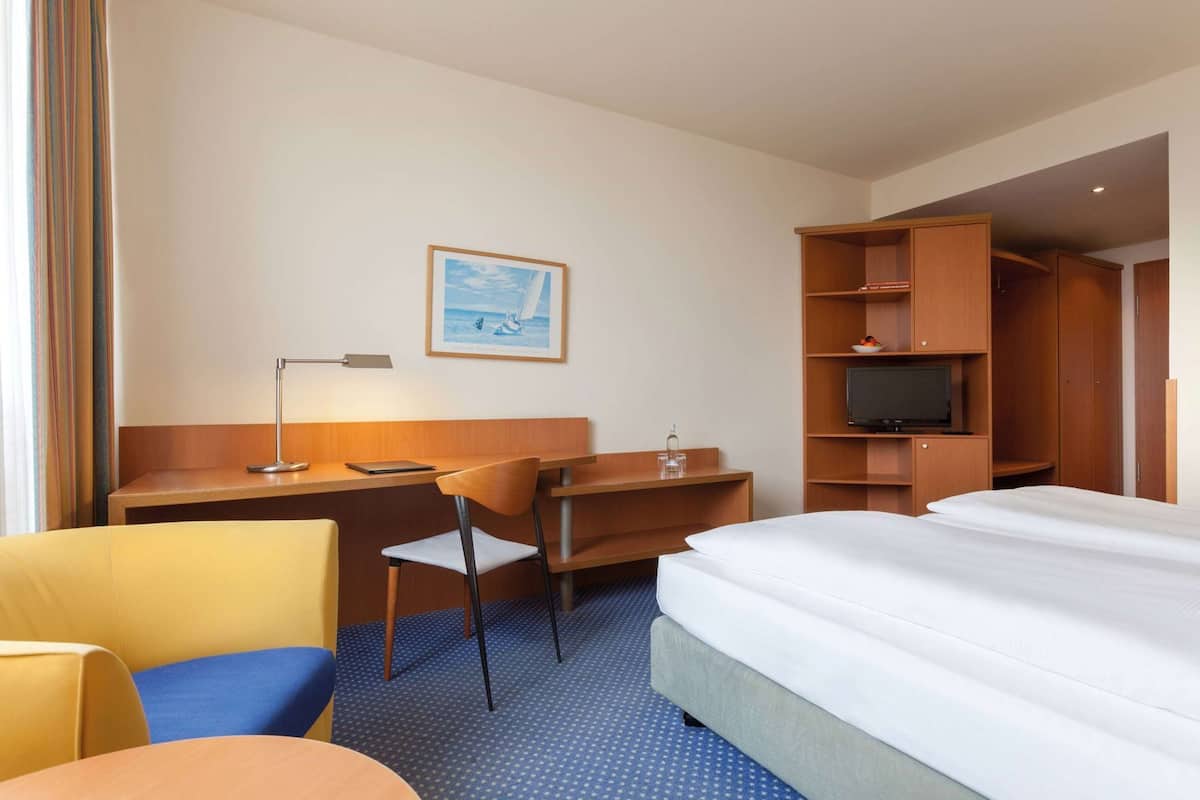 A hotel room with a bed, a desk, a chair, a television, and a wardrobe.