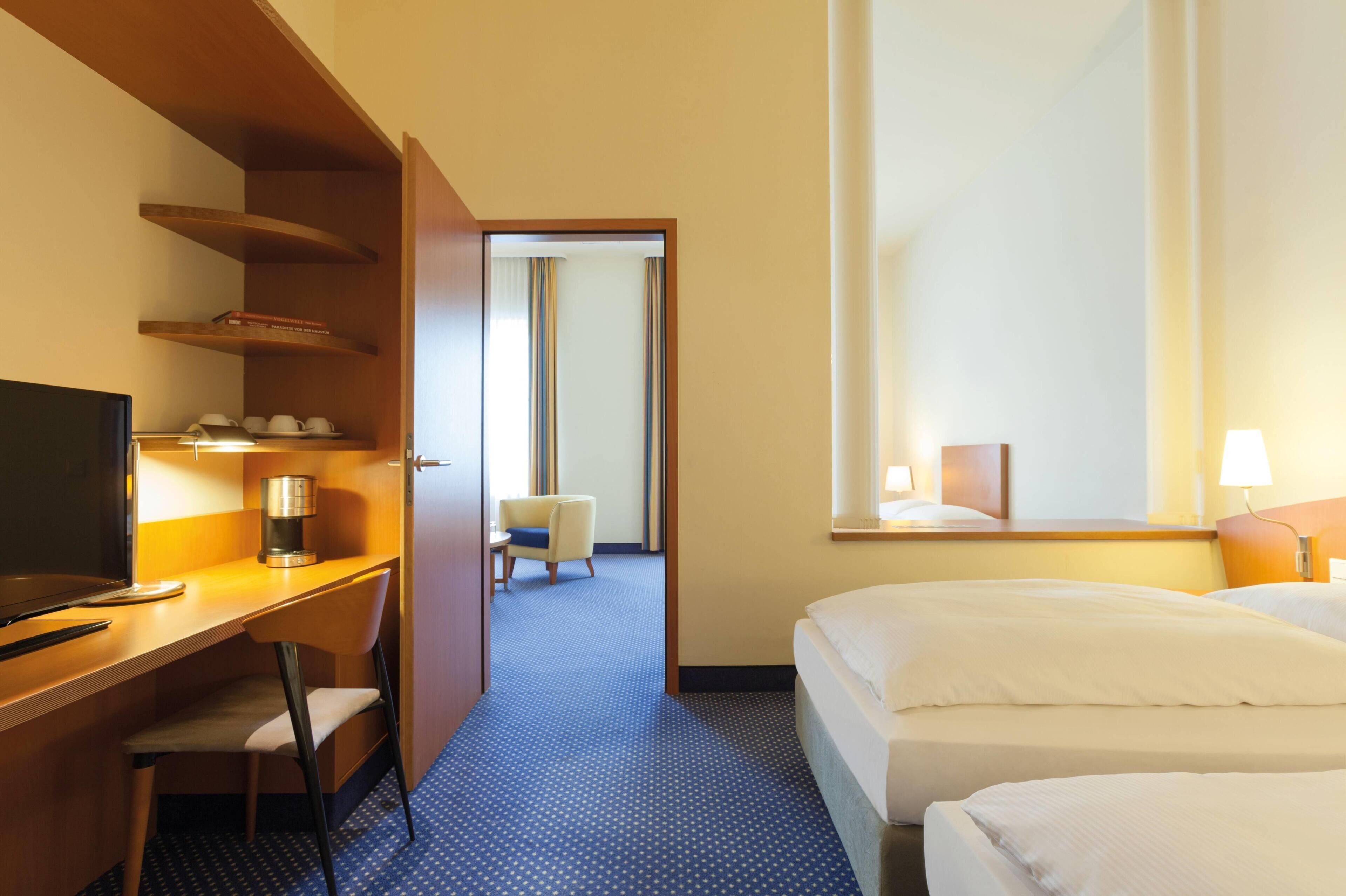 A hotel room with a desk, chair, bed, and a mirror.