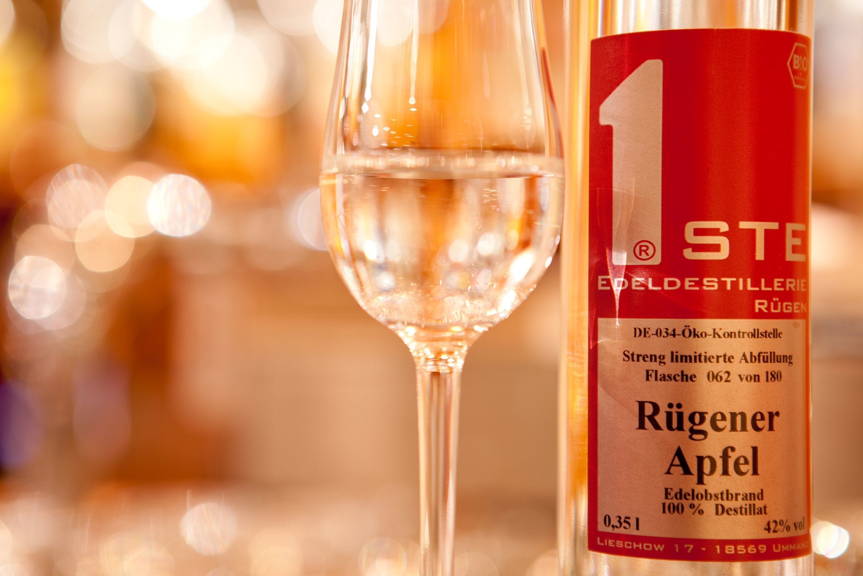 A bottle of Rügener Apfel wine with a red label and a glass of clear liquid beside it.