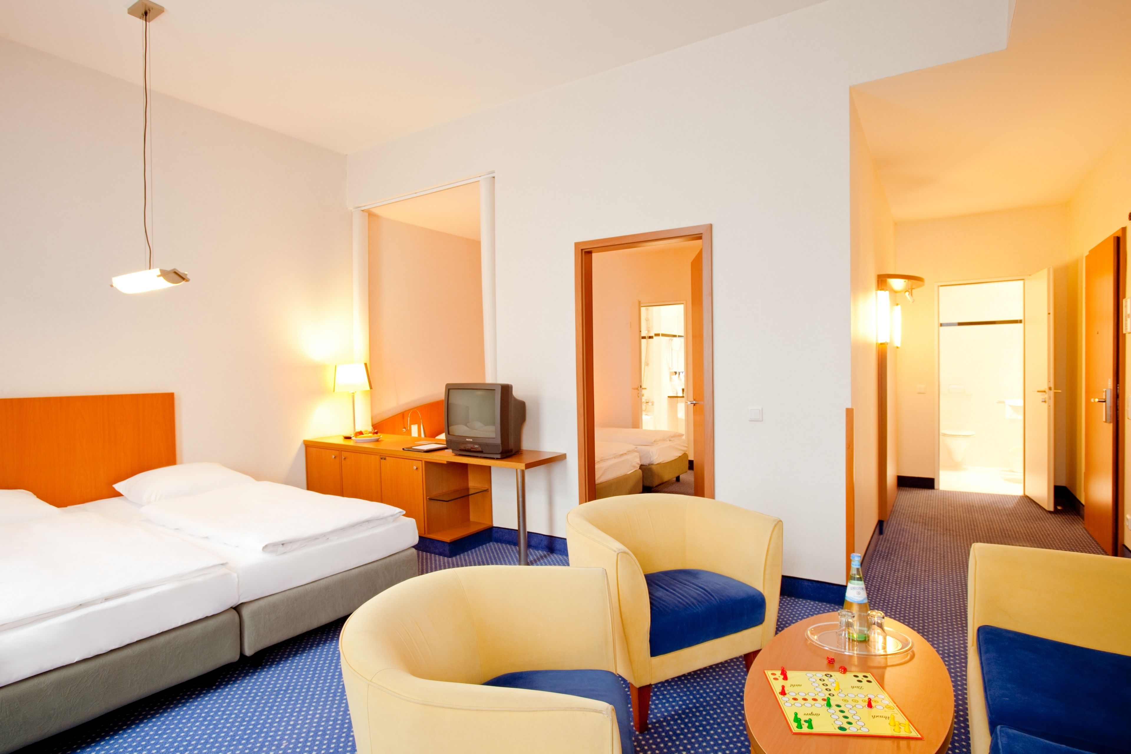 Ein Hotelzimmer mit zwei Betten, einem Schreibtisch mit Fernseher, zwei Sesseln und einem kleinen Tisch mit einem Gesellschaftsspiel.