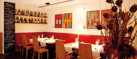 A restaurant interior with wooden chairs, tables, a chalkboard menu, and wine bottles on shelves.