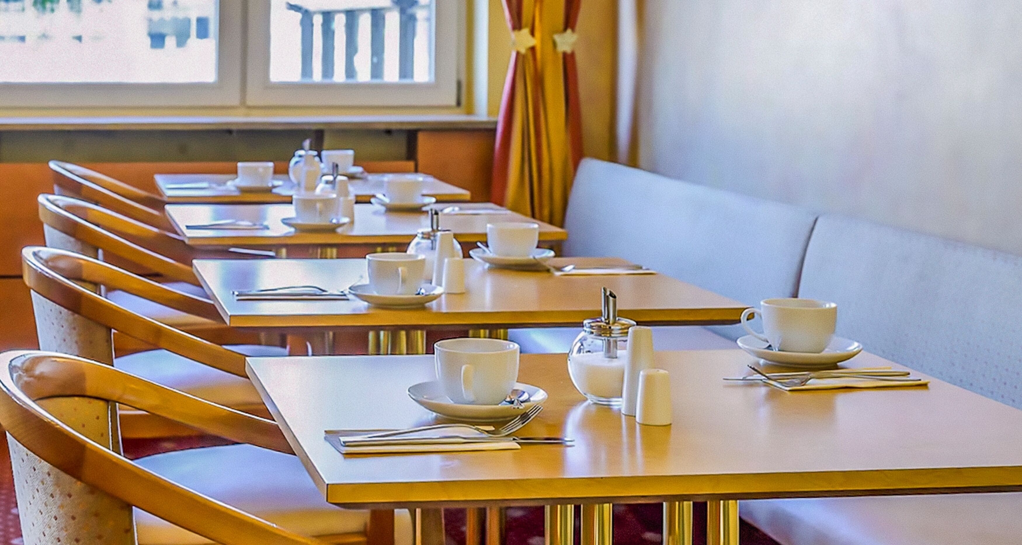 Un restaurante con varias mesas, cada una con tazas, platitos y cubiertos blancos.