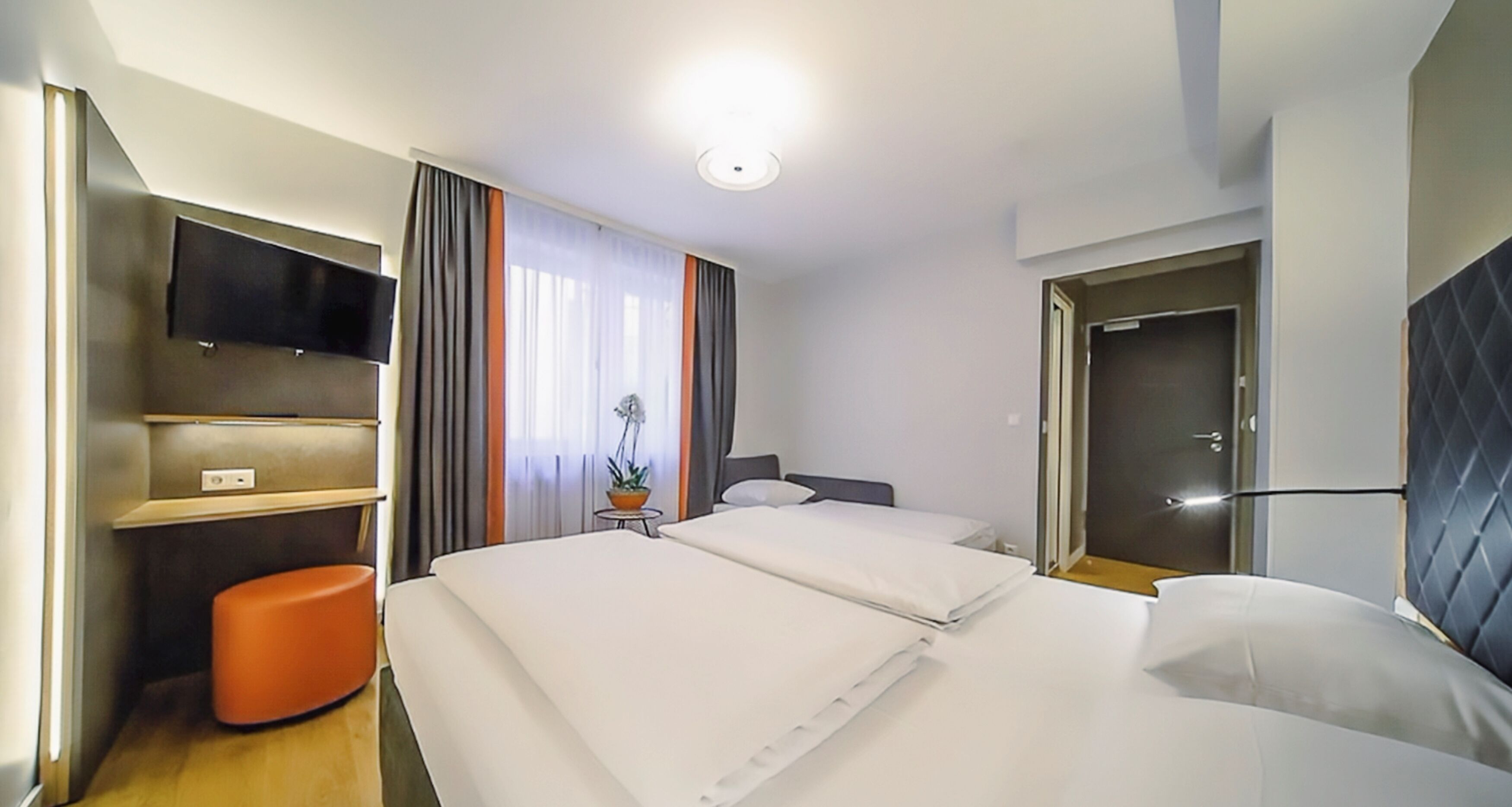 Habitación de hotel con dos camas, un televisor montado en la pared, una mesita con una planta en maceta y una puerta con manija.