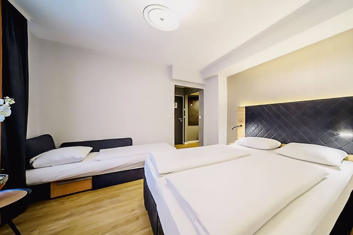 A hotel room with two beds, a wooden floor, a modern headboard, and a small table with a bowl.