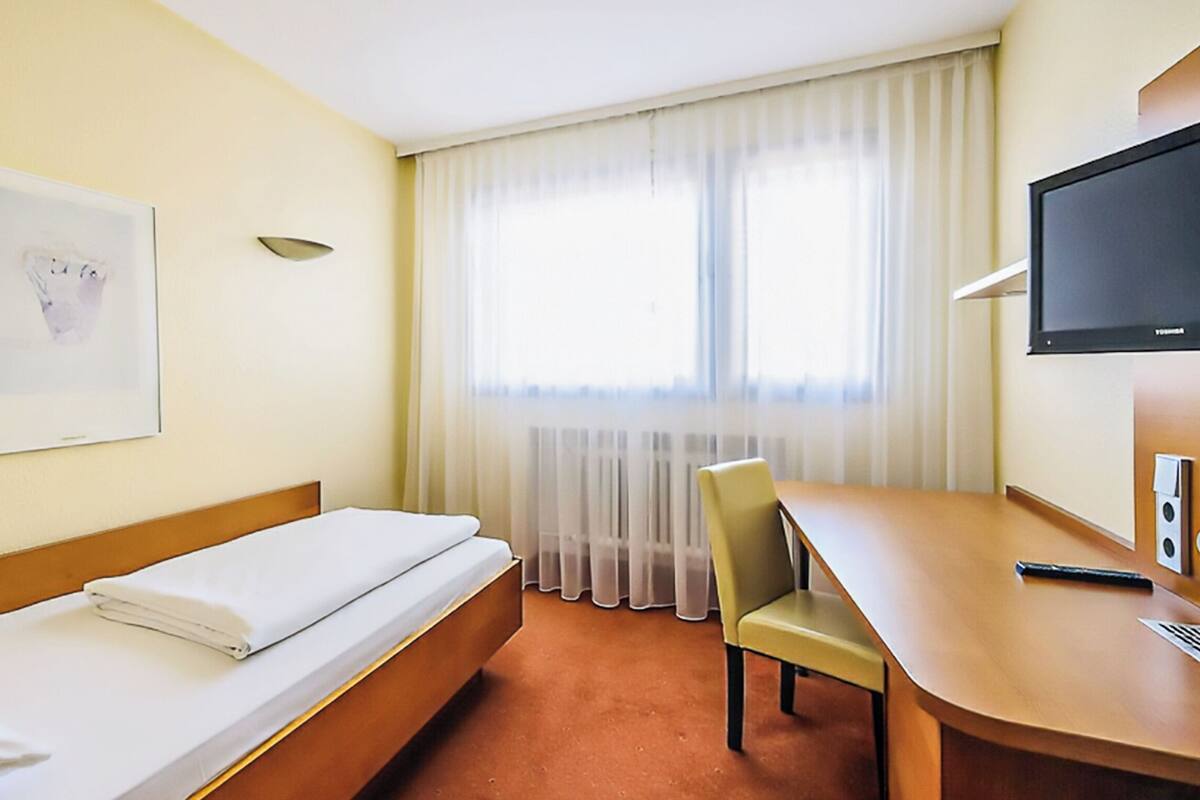 A hotel room with a bed, a desk, a chair, a television, and a window with curtains.