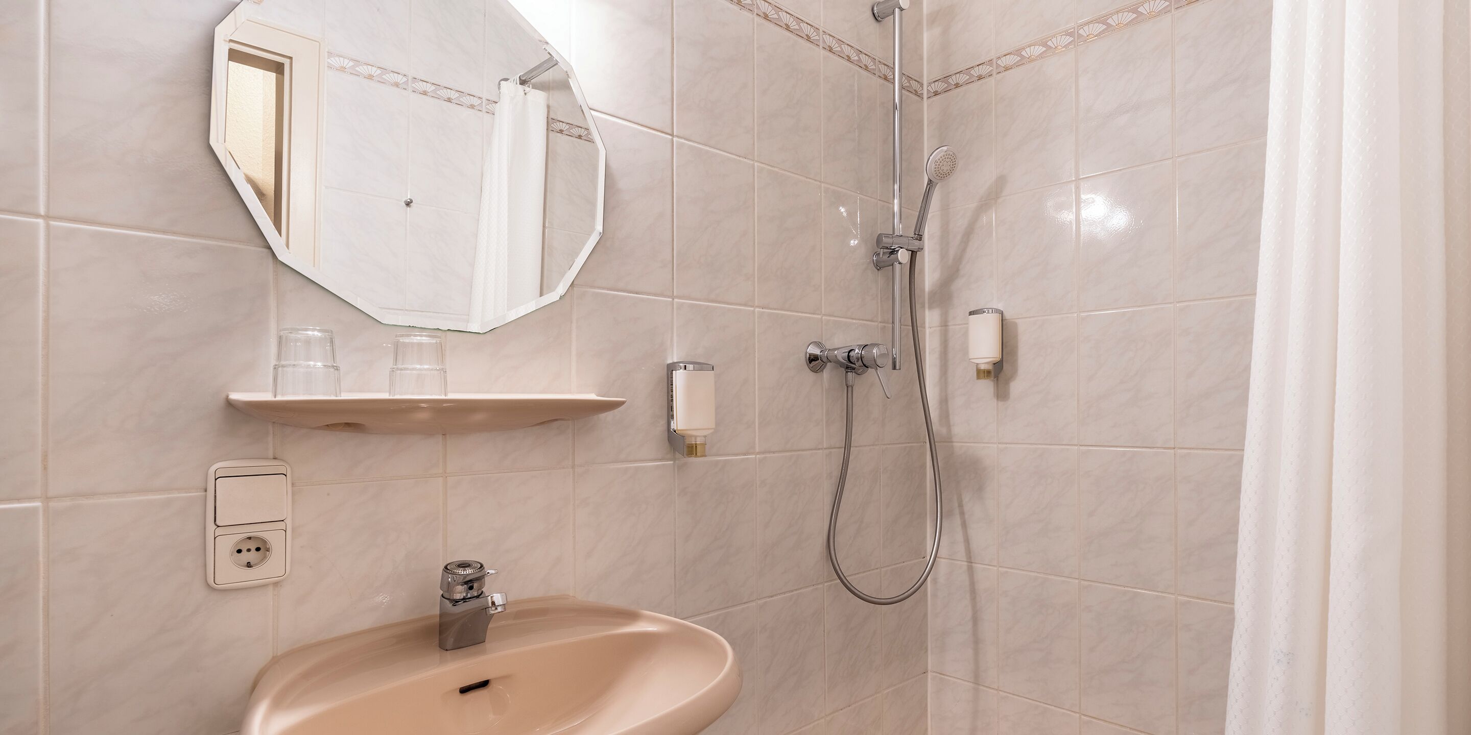 A bathroom with a sink, mirror, shower, and a towel rack.