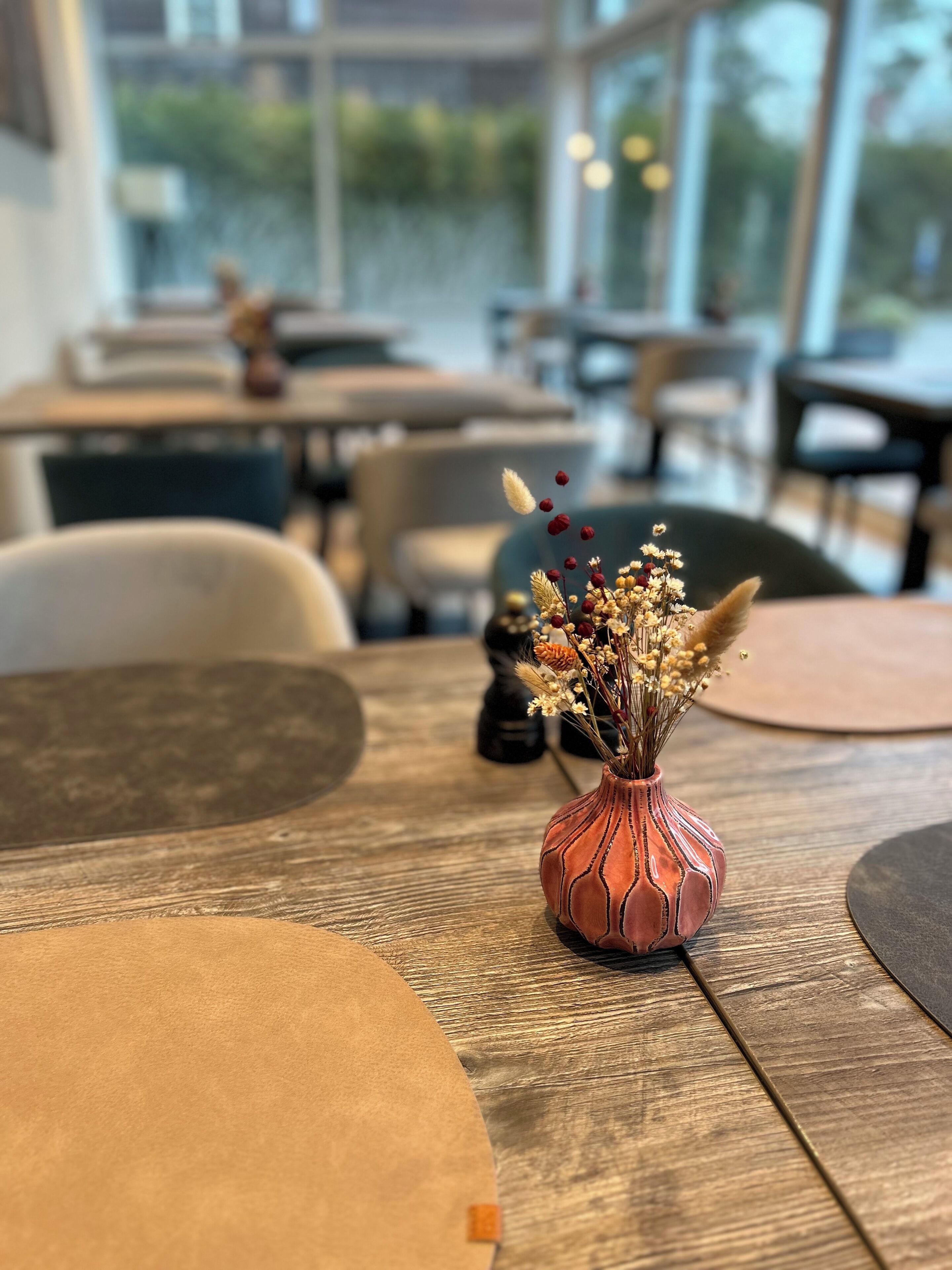 Ein Esstisch mit einer Vase getrockneter Blumen, einem schwarzen Salzstreuer und einer braunen Tischmatte.