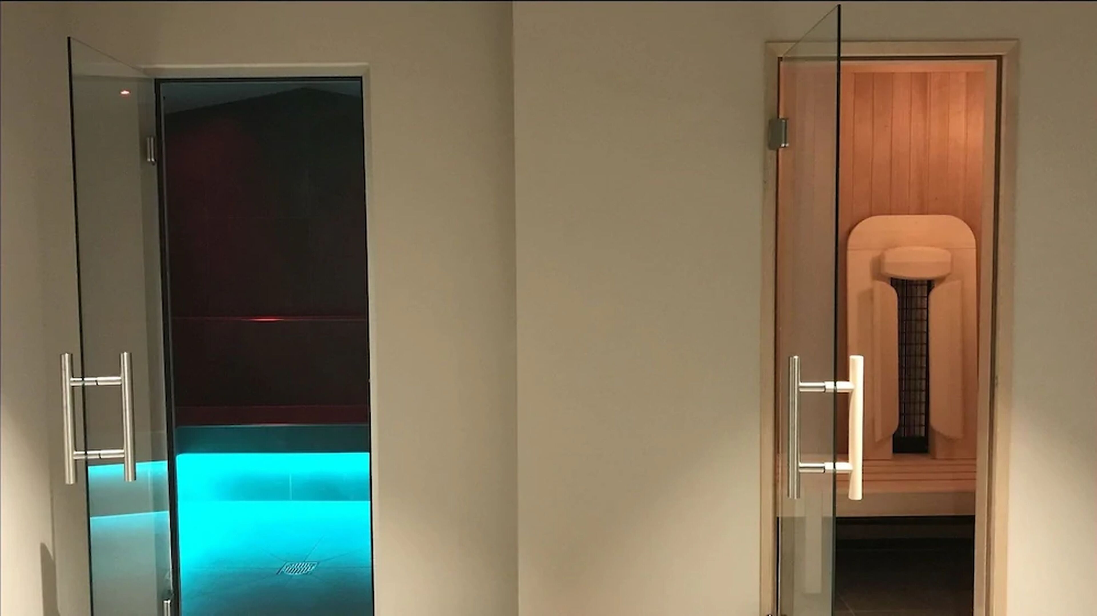 Habitación de hotel moderna con una puerta de vidrio que da al baño, una puerta de madera hacia un armario y un perchero visible.