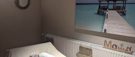 A bedroom with a bed, a wall-mounted wreath, a framed picture of a beach hut, and a radiator.