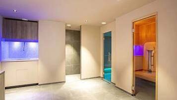 A modern hotel room with a large window, a bathroom with a blue-lit shower, and a wooden door.