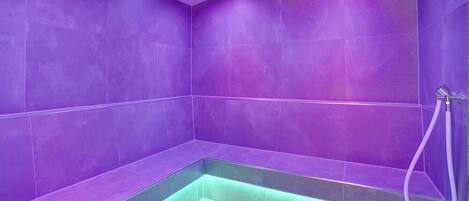 A bathroom with purple tiles and a green-lit shower area.