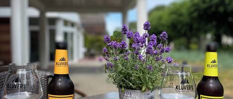 A table with two bottles of Klüver's India Pale Ale and two glasses, a potted lavender plant, and a clear sky.