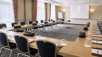 Ein Konferenzraum mit einem langen Tisch, Stühlen, einer Projektionsleinwand und einer Whiteboard-Tafel.