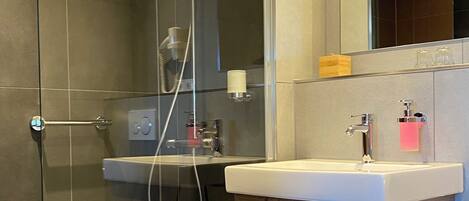 Un baño moderno con ducha de vidrio, lavamanos blanco y tocador de madera.