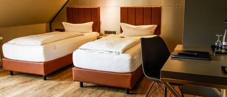 A modern hotel room with two beds, a wooden floor, and a desk with a chair.