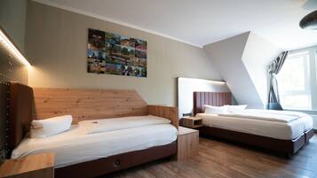 A modern bedroom with two beds, wooden headboards, a wall art collage, and a sloped ceiling.