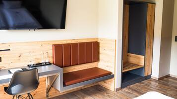 A modern hotel room with a bed, a desk, a chair, a TV, and a wooden bench.