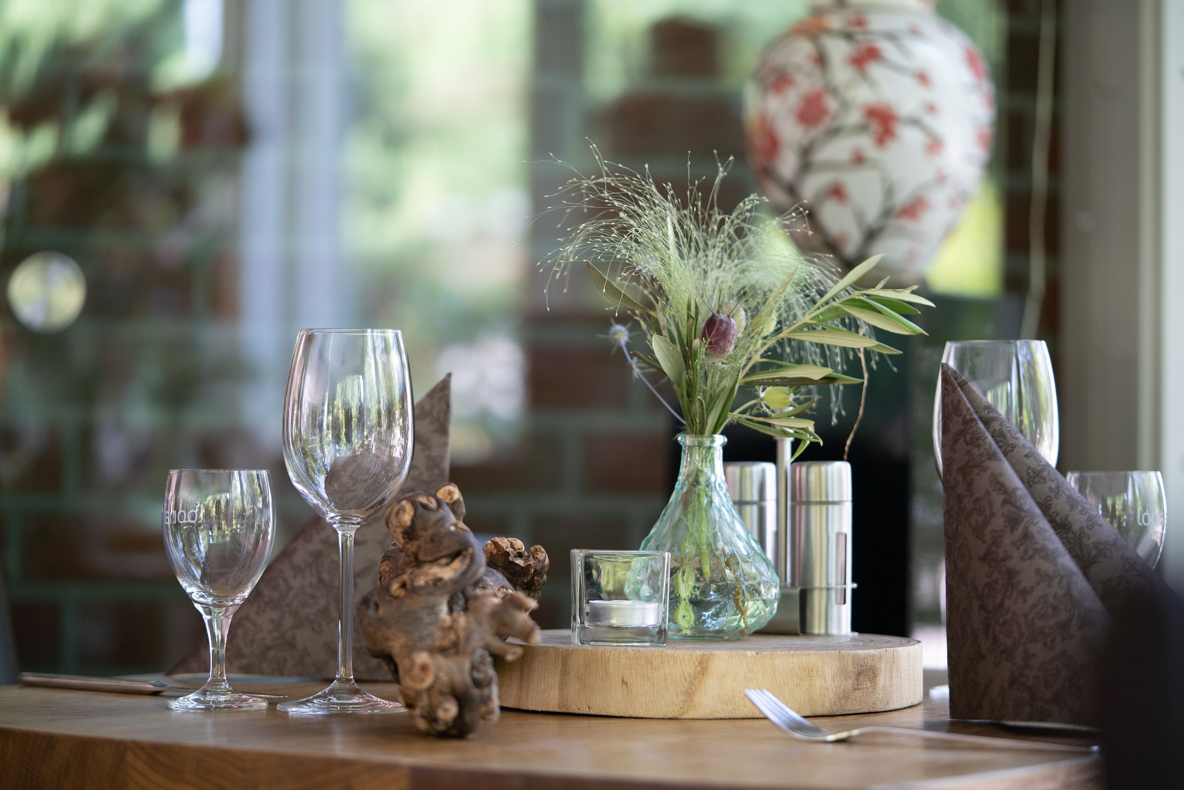 A table with two wine glasses, a vase with dried plants, a candle, and a decorative item.