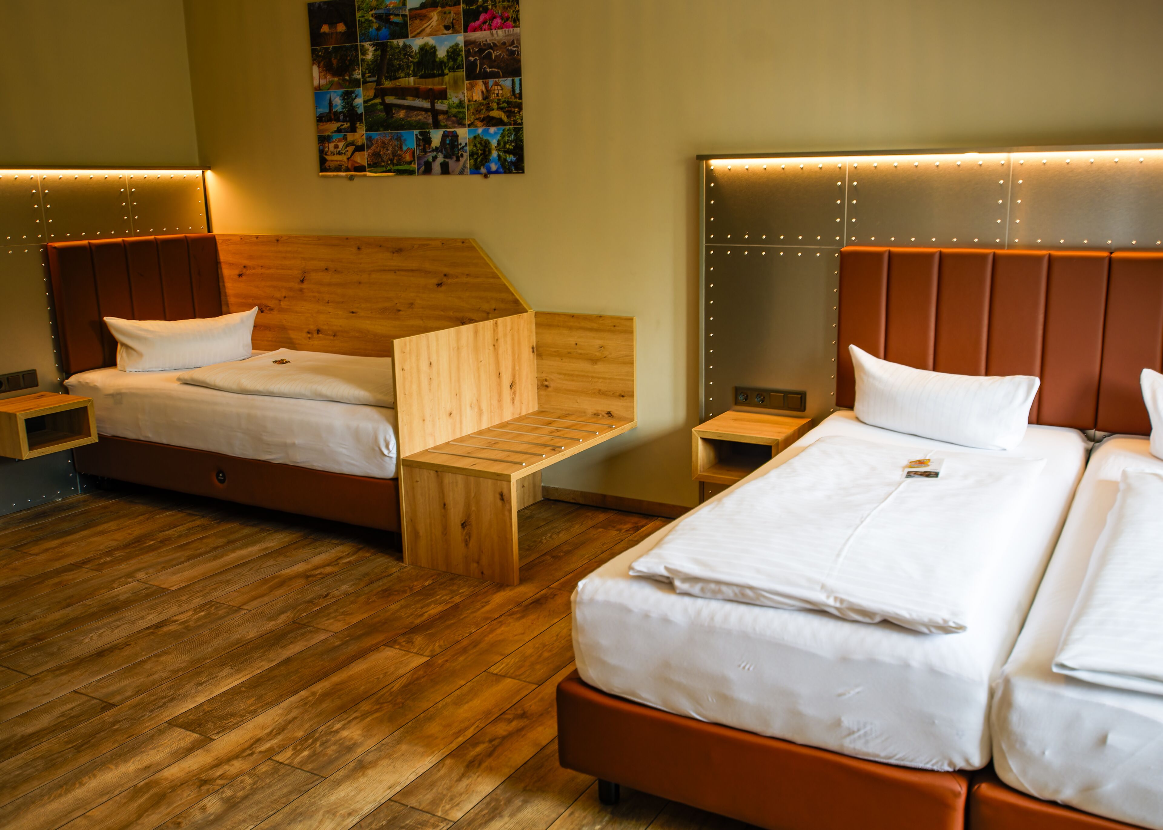 Quarto de hotel com duas camas, cabeceiras de madeira, um pequeno banco de madeira e uma colagem de fotografias na parede.