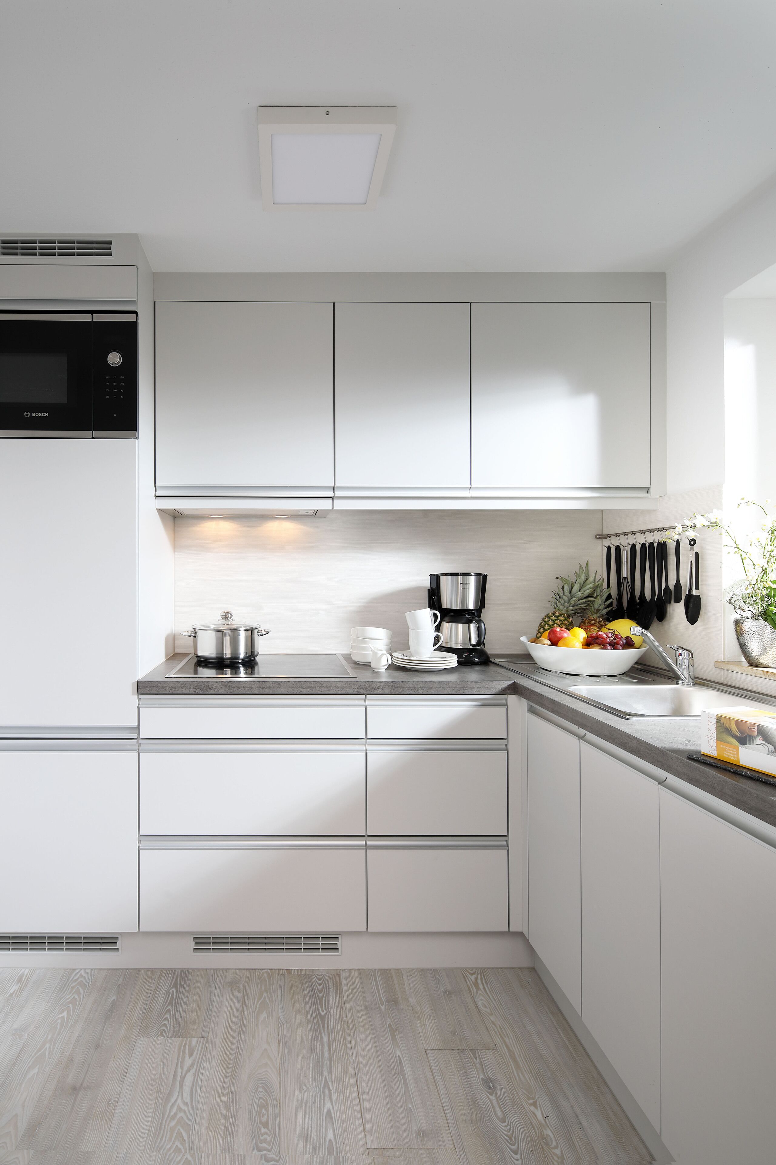 A modern kitchen with white cabinets, a Bosch microwave, a coffee maker, and a fruit bowl.