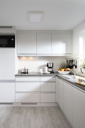 Una cocina moderna con armarios blancos, un microondas Bosch, una cafetera y un frutero.