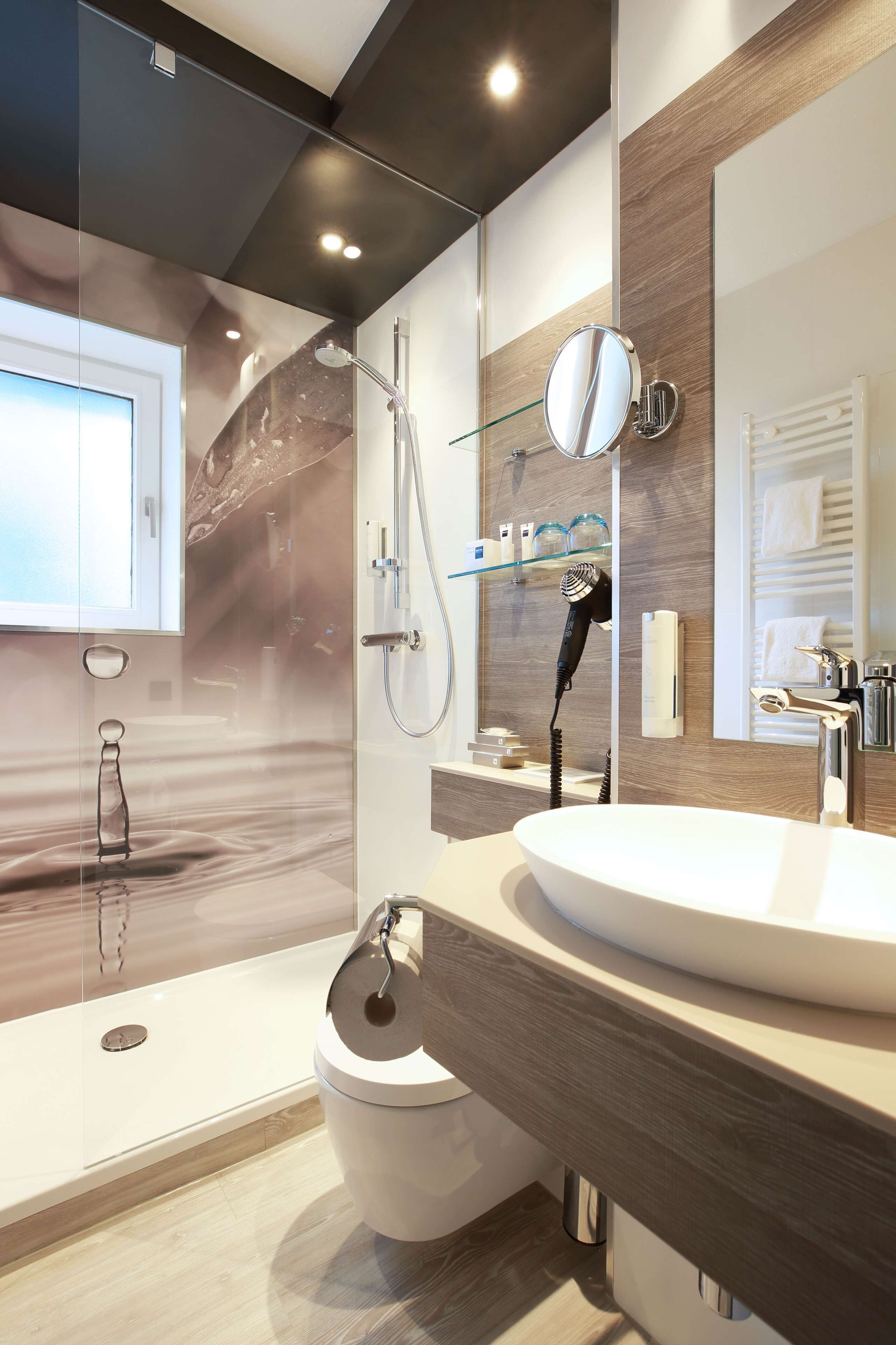 Een moderne badkamer met een grote spiegel, een rond wastafel en een douche met glazen wanden.