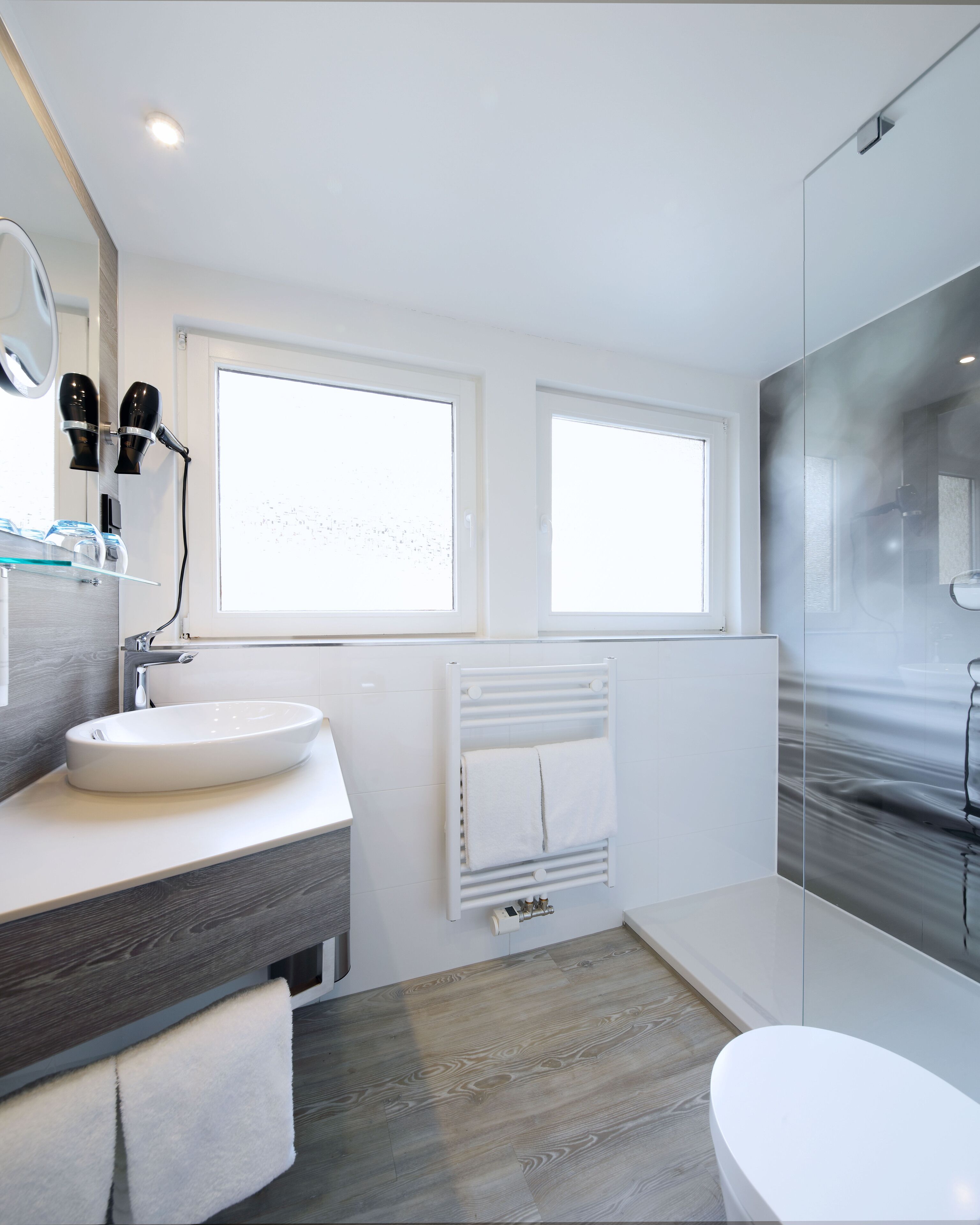 A modern bathroom with a white sink, vanity, and a glass shower enclosure.