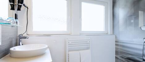 A modern bathroom with a white sink, vanity, and a glass shower enclosure.
