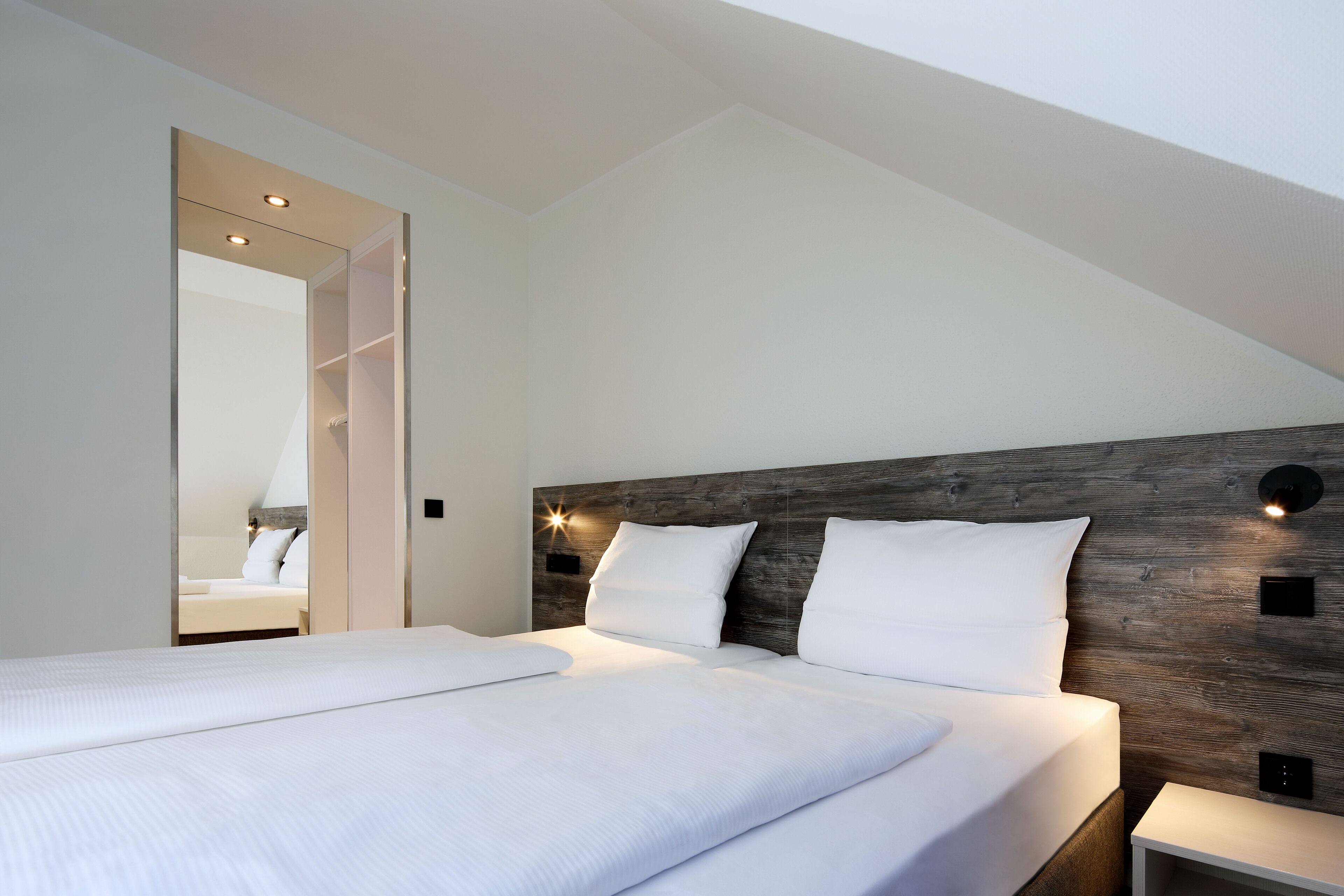 A modern bedroom with a large bed, wooden headboard, and built-in lighting.