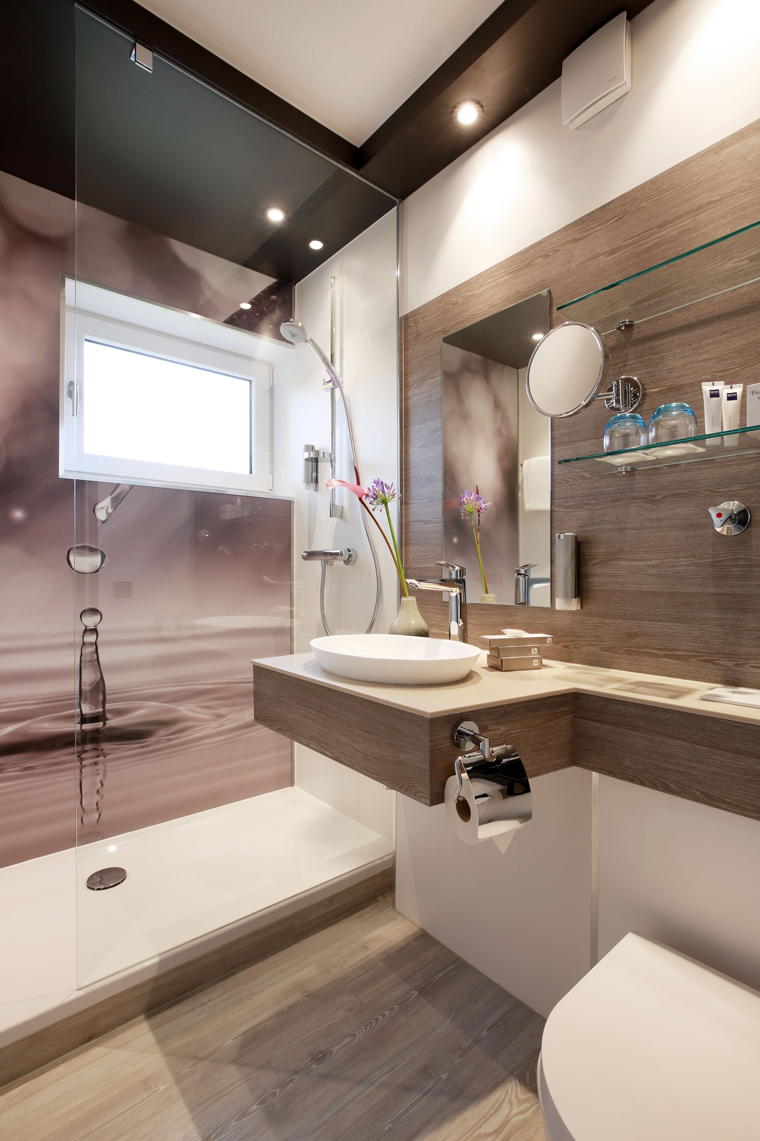A modern bathroom with a glass shower enclosure, a large mirror, and a wooden vanity.