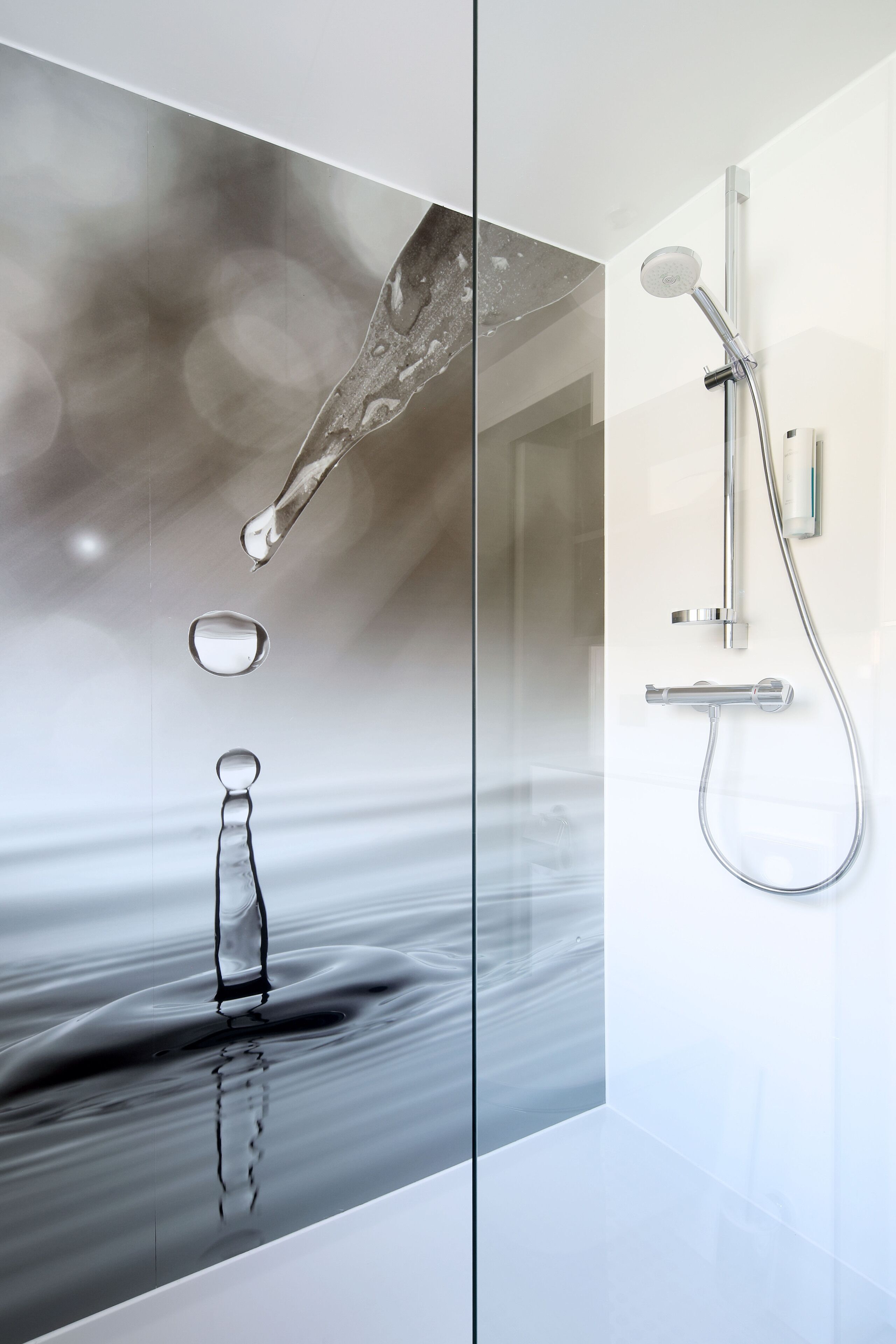 A modern bathroom with a glass partition, a shower with a handheld showerhead, and a clear glass bottle with water droplets.
