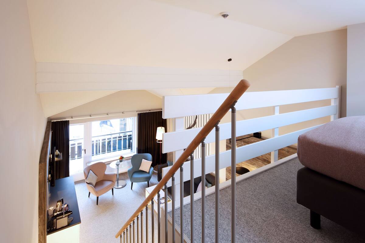 A modern hotel room with a staircase, a balcony, and a seating area with a table and chairs.
