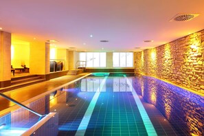 Una piscina interior moderna con pared de piedra y barandilla de vidrio.