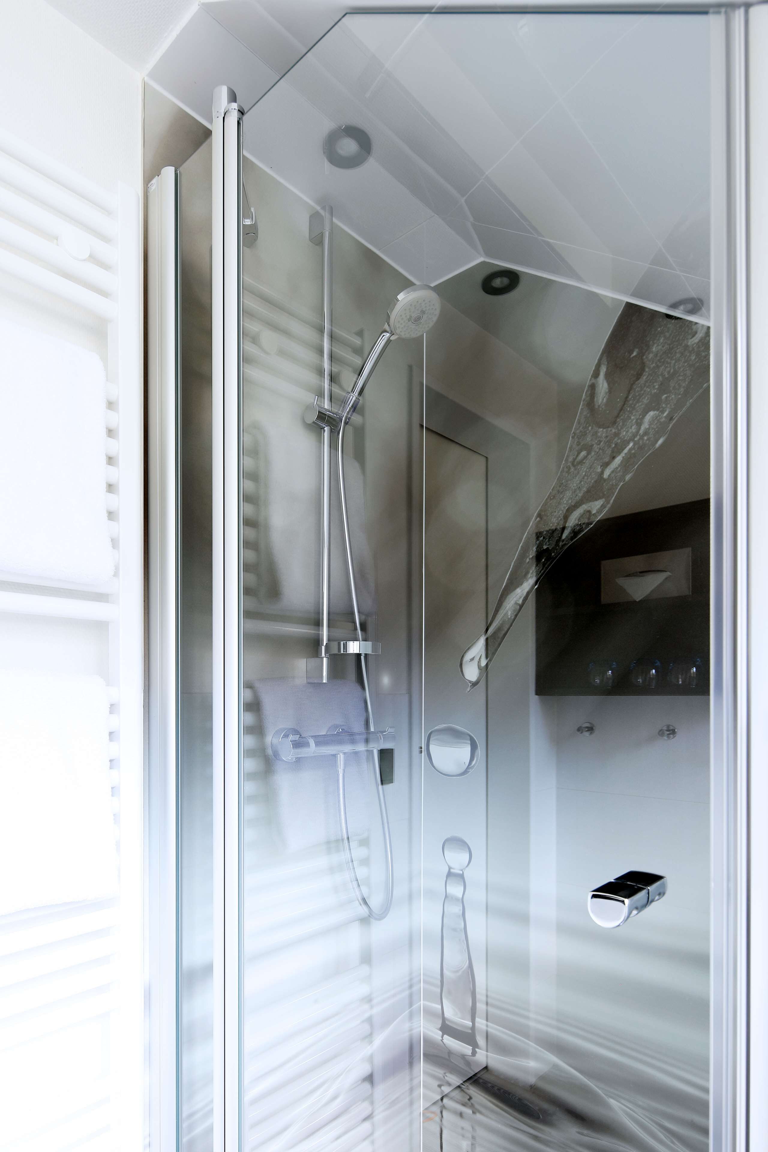 A modern bathroom with a glass shower enclosure, a towel rack, and a soap dispenser.
