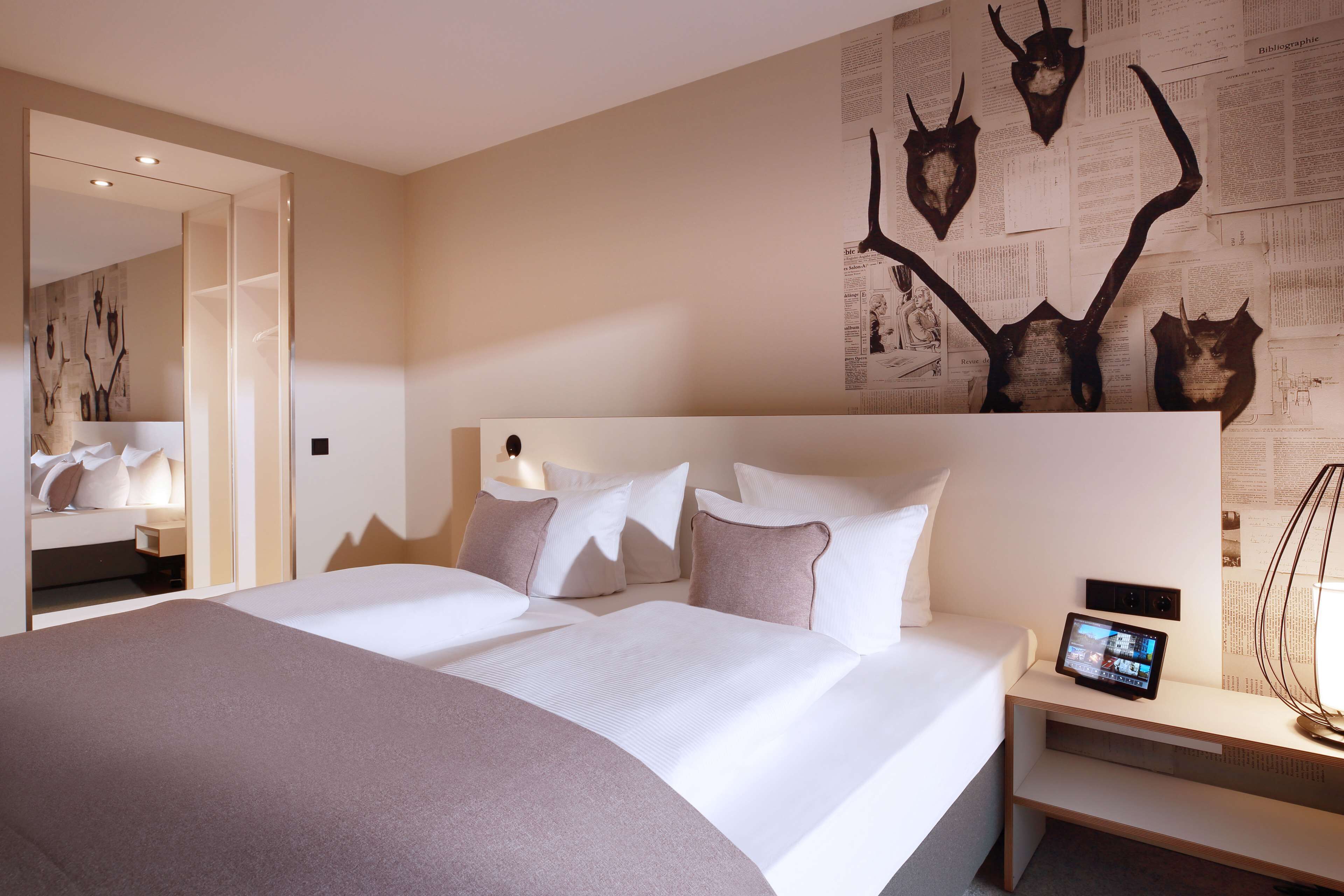 Ein modernes Hotelzimmer mit einem großen Bett, einem Nachttisch mit einem Tablet und einer Wand, die mit Tierschädeln dekoriert ist.