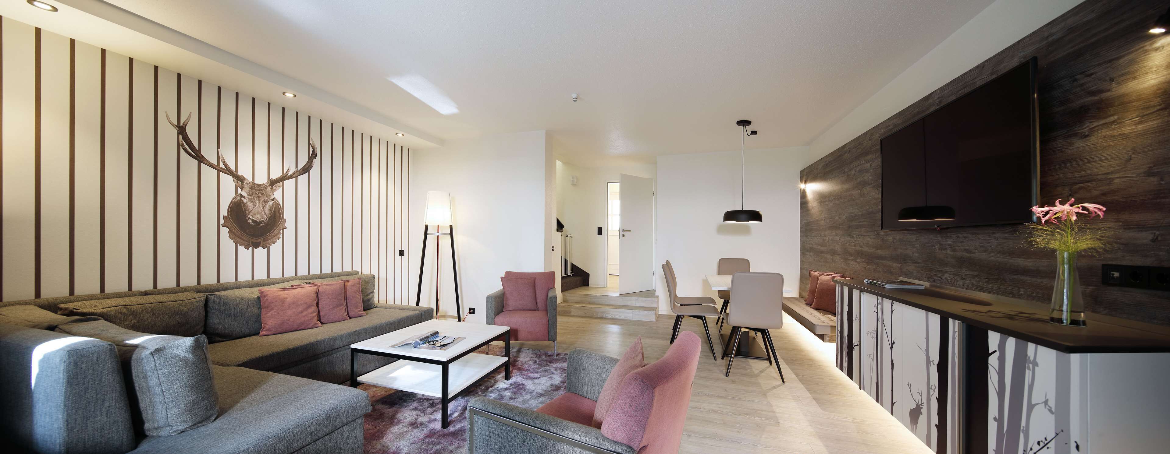 Una sala de estar moderna con un sofá, sillas, una mesa de centro, una chimenea y una cabeza de ciervo montada.