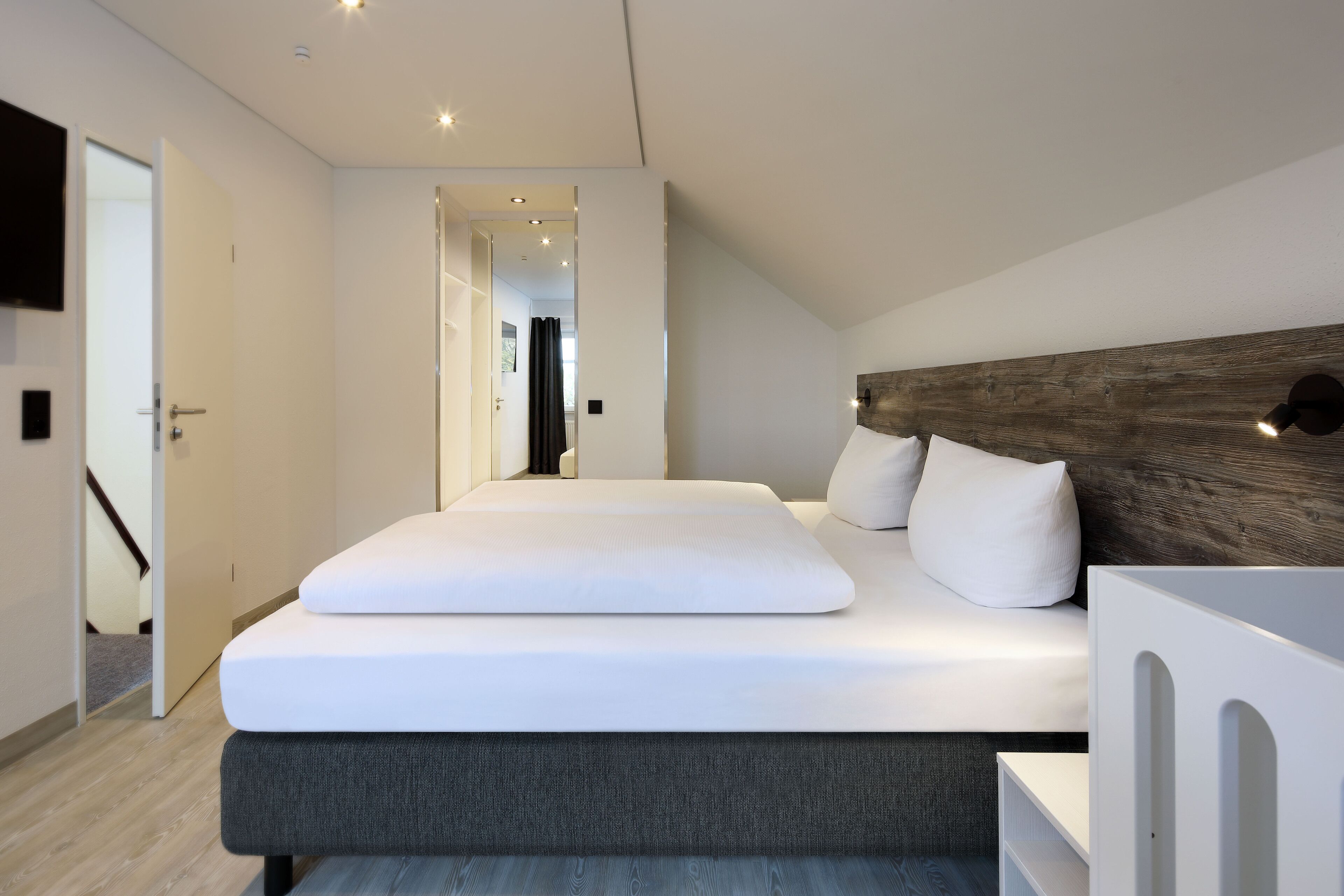 A modern bedroom with a large bed, a wooden headboard, and a white bedside table.