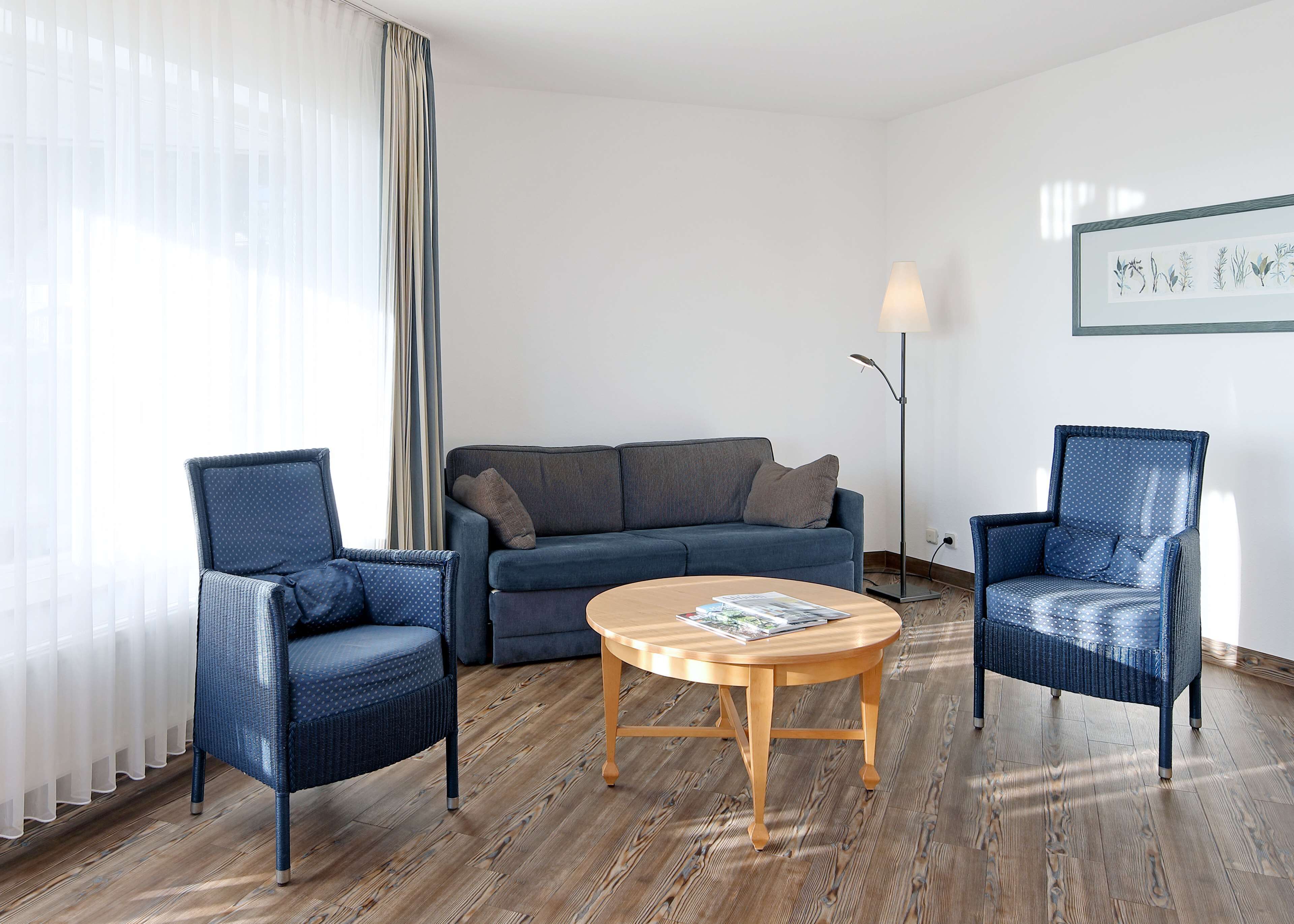 Een moderne woonkamer met een blauwe bank, twee blauwe fauteuils, een houten salontafel en een vloerlamp.