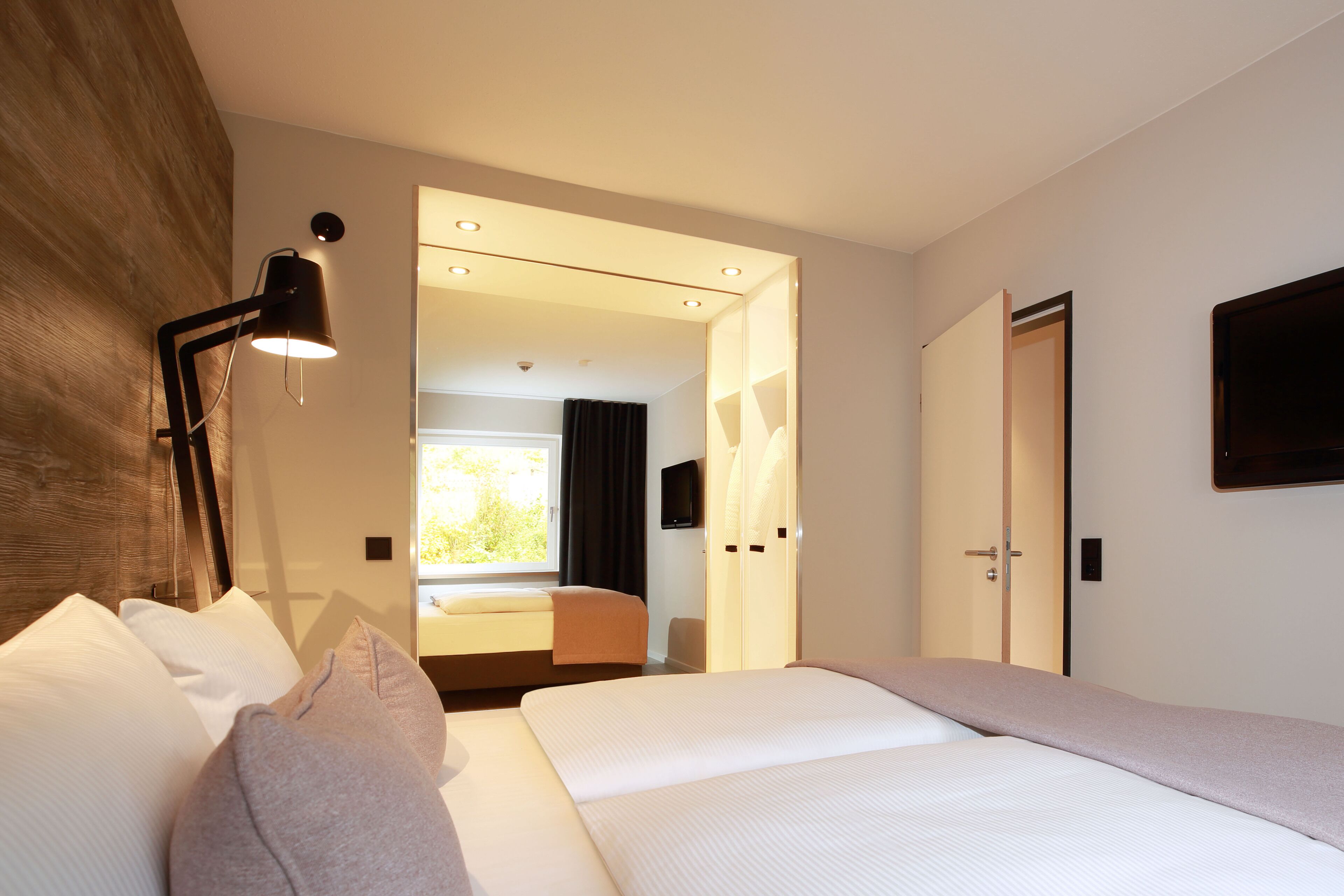A modern hotel room with a large bed, a bedside lamp, a flat-screen TV, and a view of the outdoors through an open door.