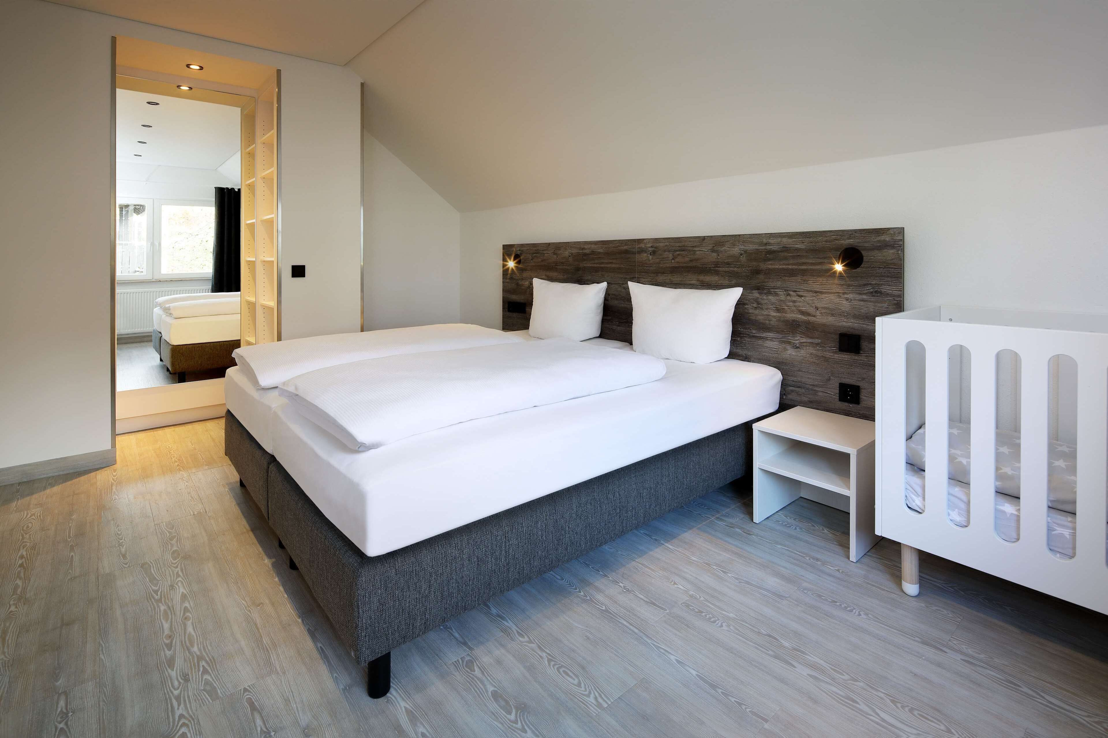 A modern bedroom with a large bed, a wooden headboard, and a white crib.