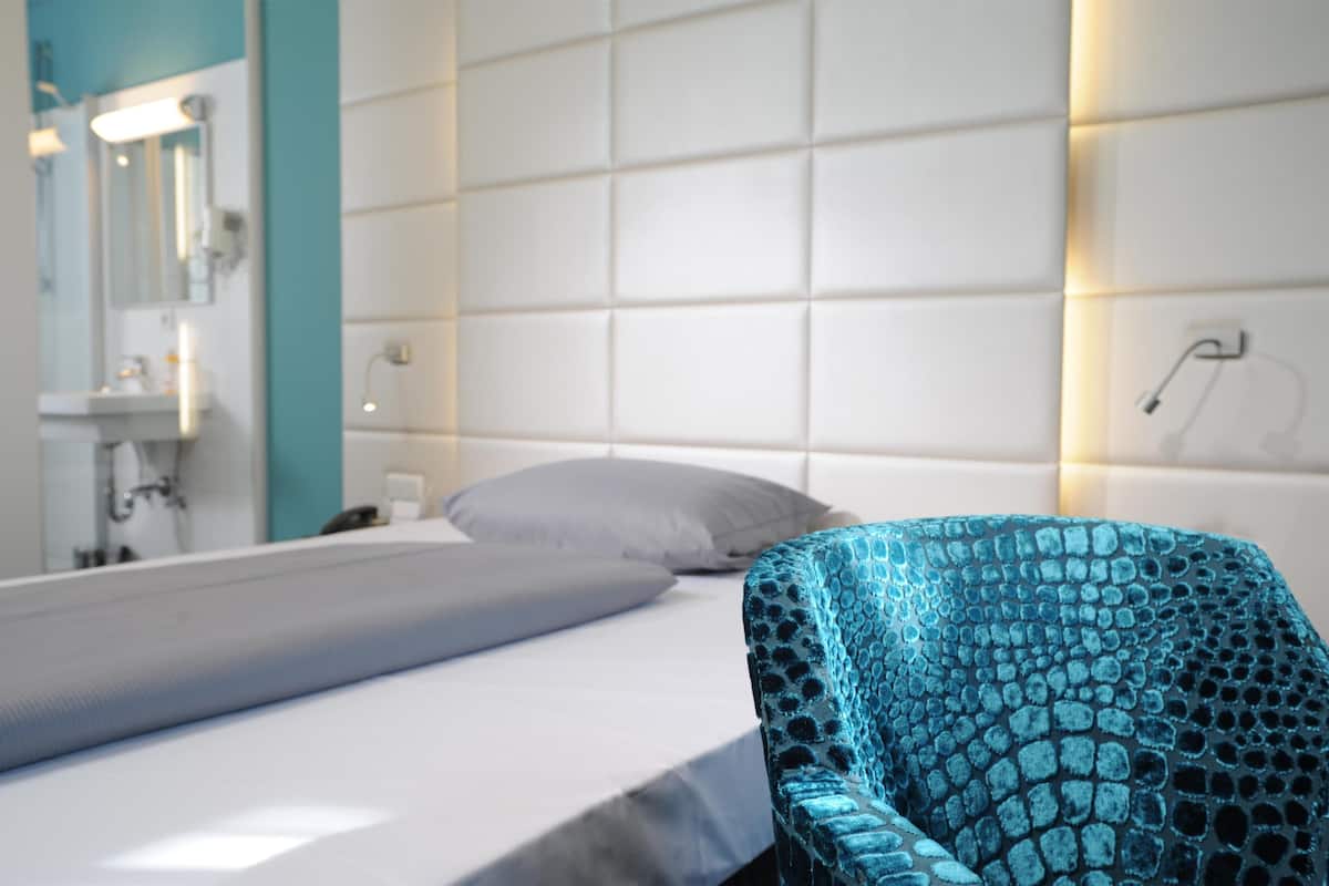 Ein Hotelzimmer mit Bett, Badezimmer mit Spiegel und einem blauen Stuhl mit Muster.