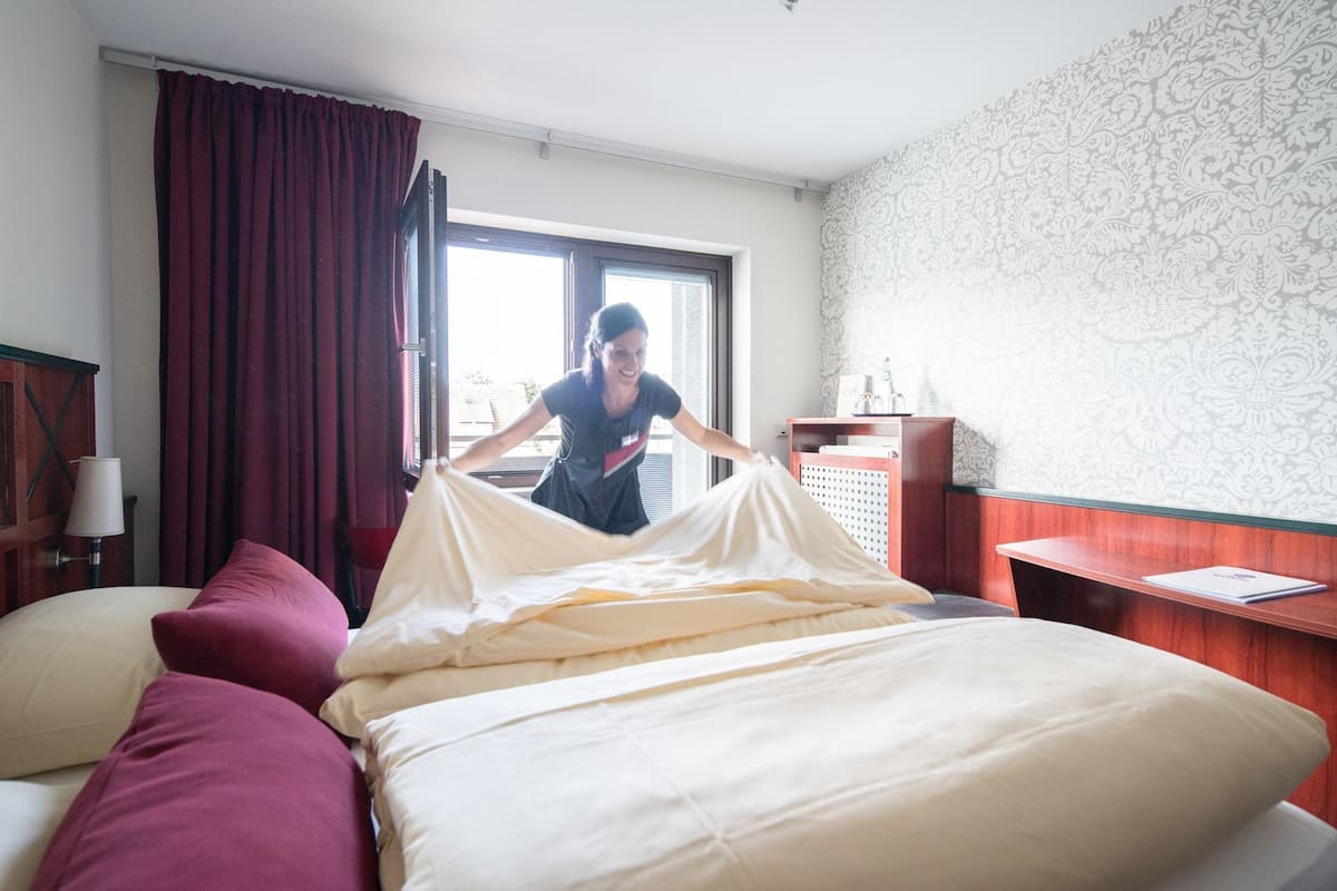 Ein Hotelzimmer mit Bett, Schreibtisch, Lampe und einem fensterbepflanzten Fenster.