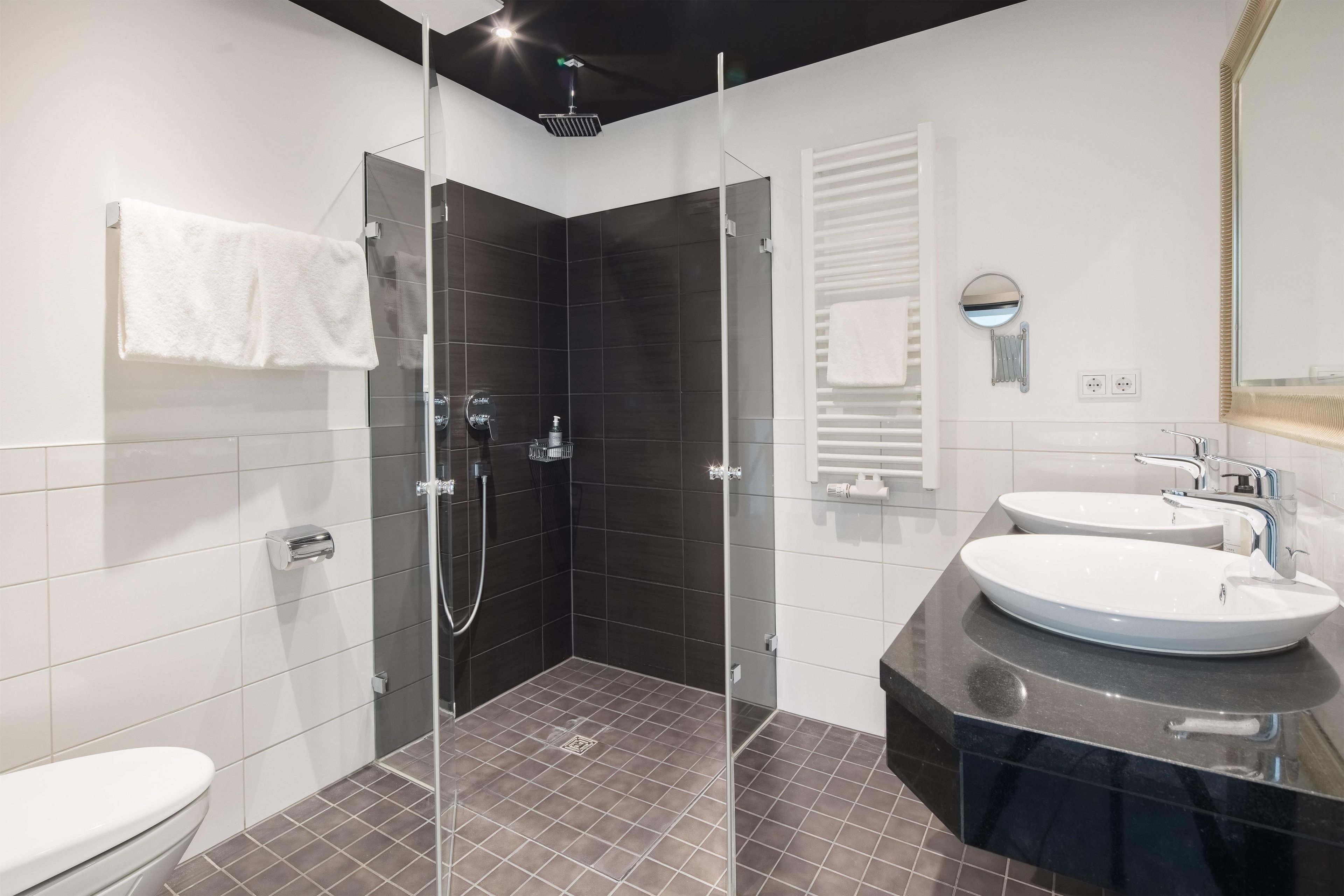 Ein modernes Badezimmer mit einer gläsernen Dusche, zwei Waschbecken und einer Toilette.